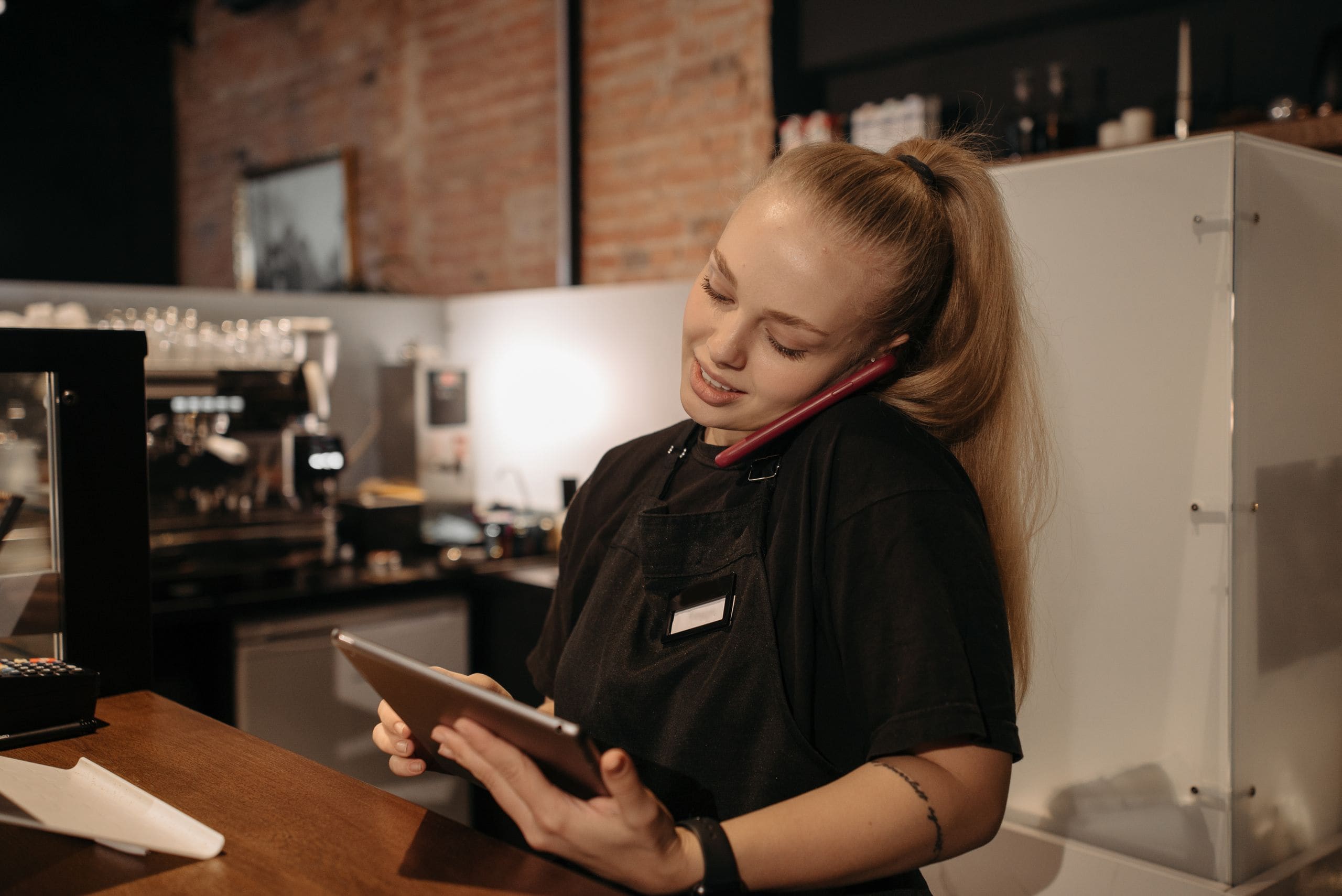 A cafe owner taking an order by phone at the counter, tablet in hand