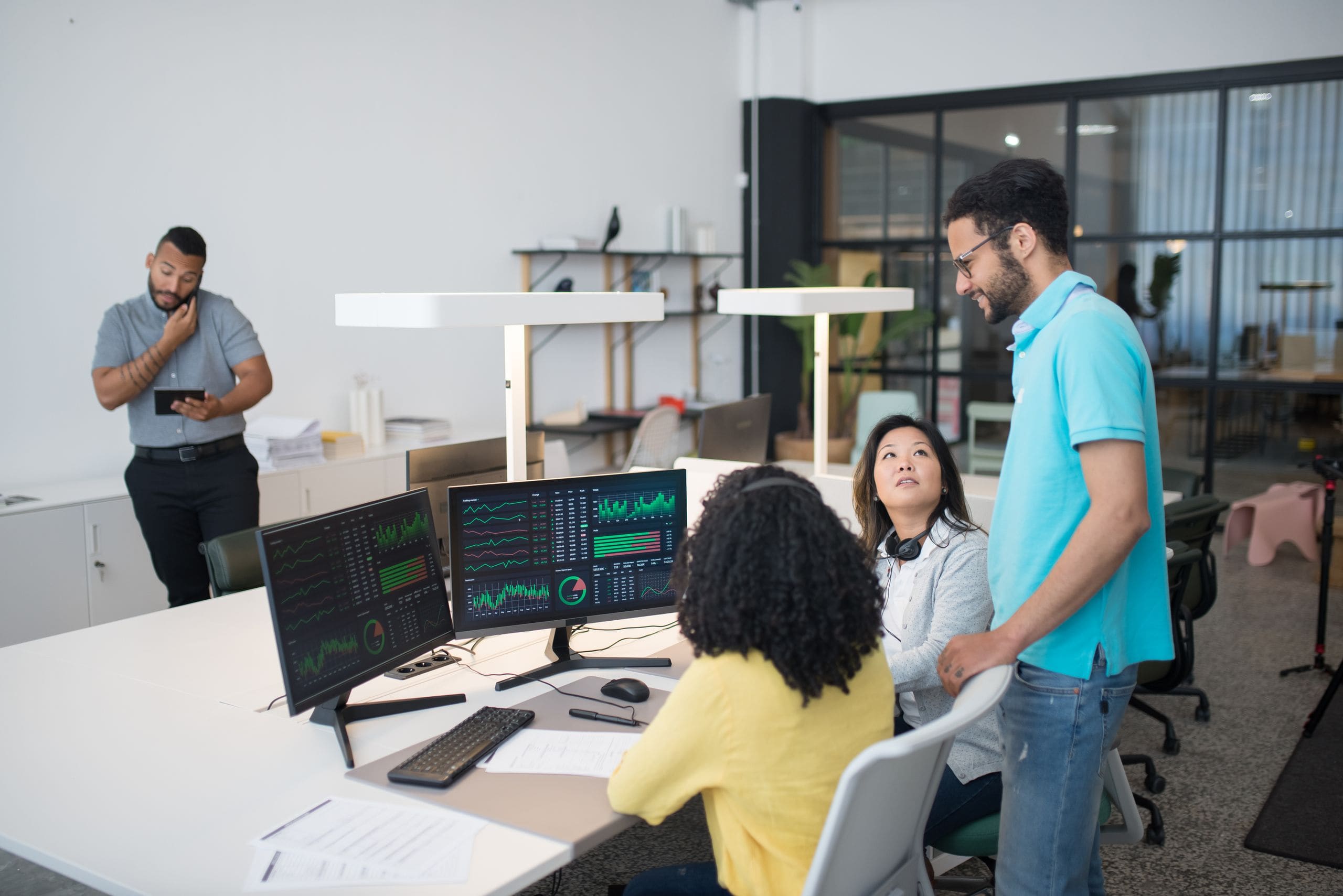 An office team gathered around two monitors of live business charts