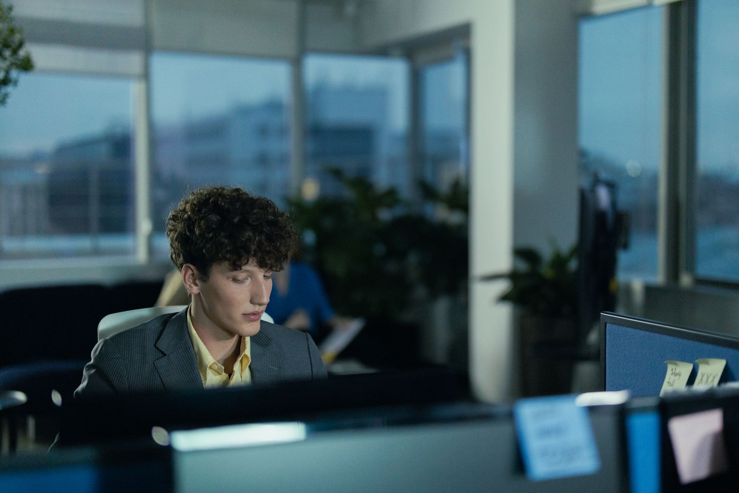 An engineer working late at his desk as the office windows turn blue at dusk