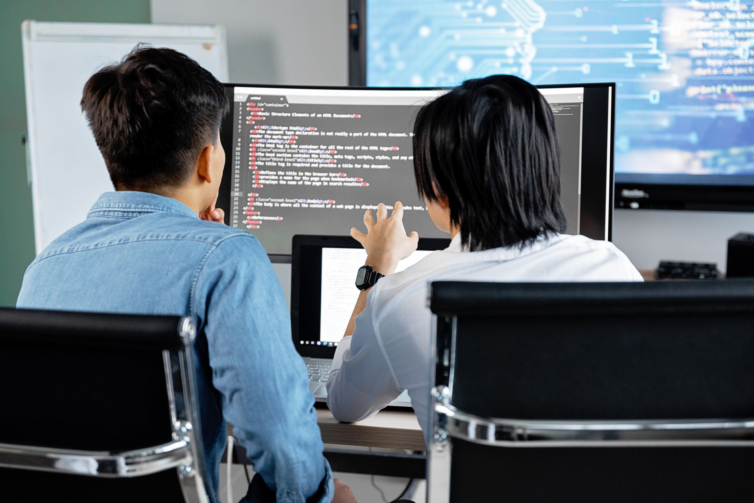 Two engineers reviewing code together on a large monitor