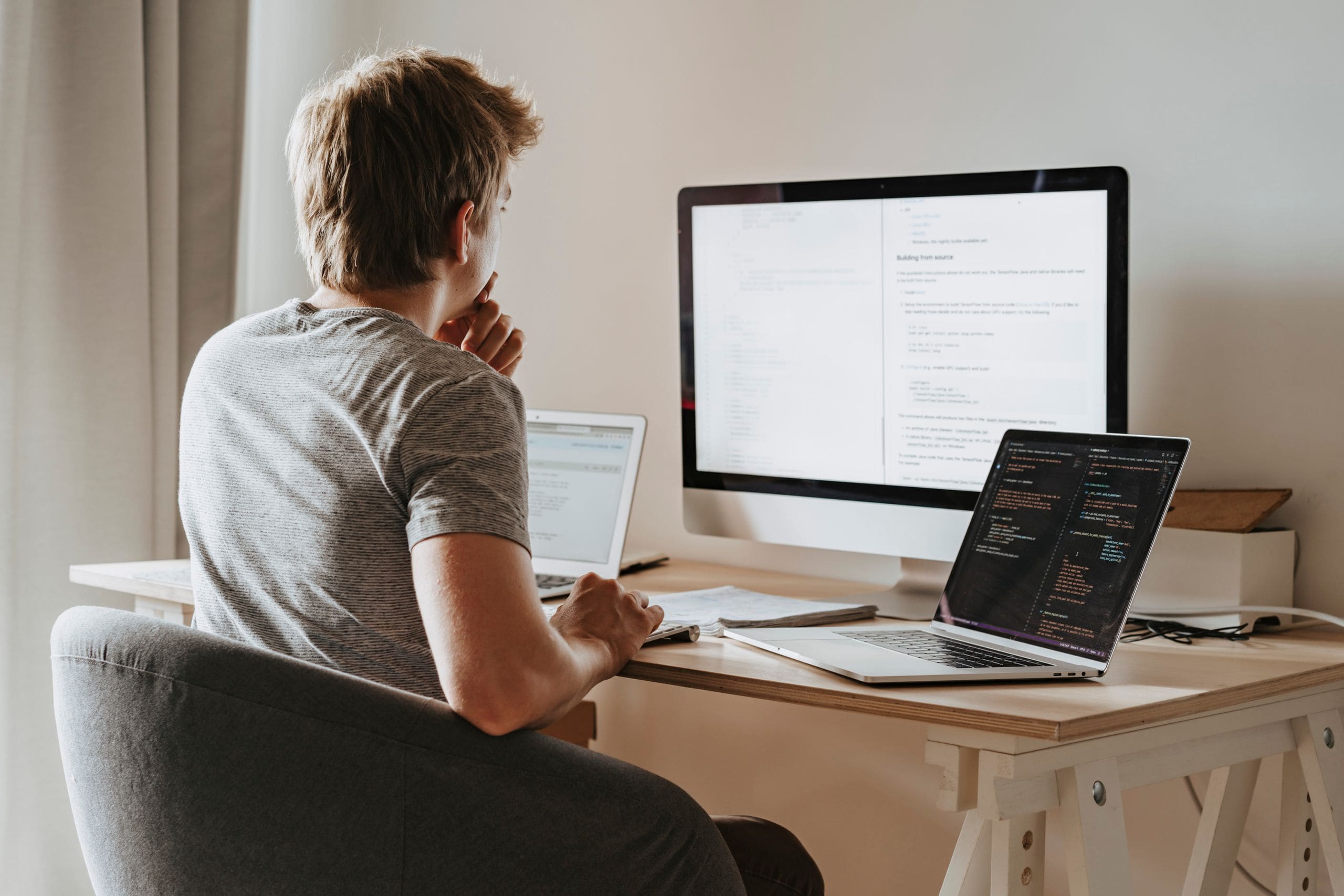 An engineer at a desk with a laptop and a large monitor, working through code