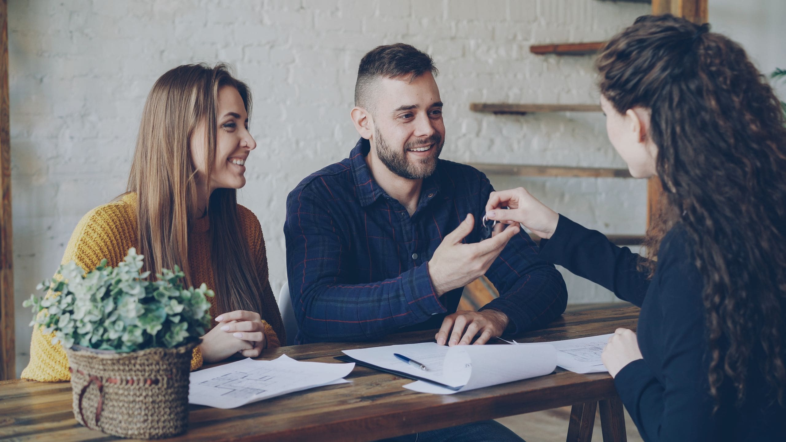 A smiling couple receiving their keys from an agent across a wooden desk